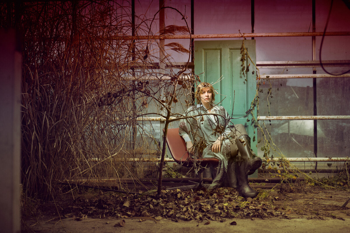 Kvinne som sitter i en stol foran et gjengrodd drivhus